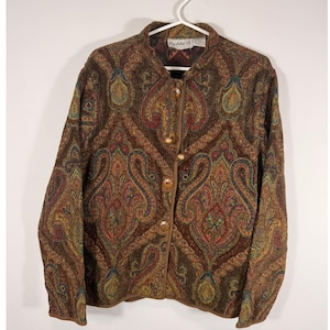 Puede incluir: Una chaqueta de manga larga con un estampado de cachemir multicolor en tonos marrón, rojo, verde y dorado. La chaqueta tiene un cuello alto, un cierre frontal con cuatro botones redondos y texturizados, y una etiqueta que dice Flashback.
