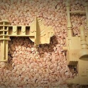 May include: Two beige plastic toy pieces, one with a long, straight bar and a curved end, and the other with a tall, rectangular shape with a rounded top and a series of vertical lines.