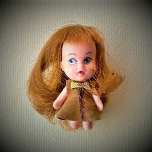 May include: A small vintage doll with brown hair and a brown dress. The doll has blue eyes and a painted face.