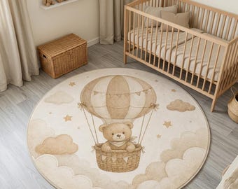 May include: A round area rug featuring a beige and cream illustration of a teddy bear riding in a hot air balloon. The design includes soft clouds and small stars surrounding the balloon, rendered in neutral earth tones on a circular fabric base.