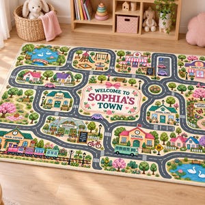 May include: A rectangular play rug featuring a colorful town map with roads, a train station, a school, a library, a greenhouse, and a park. The center displays the text Welcome to Sophia's Town surrounded by floral illustrations and a pink bow.