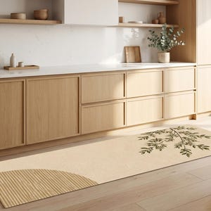 May include: A long rectangular runner rug featuring a light beige base colour. One end displays a textured semi-circular pattern with vertical lines, while the opposite end features a dark green botanical branch illustration with detailed leaves.