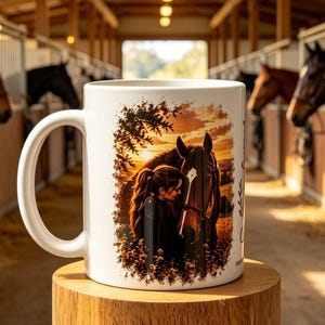以下が含まれることがあります： 夕暮れ時に馬の隣に立つ人物のイラストがプリントされた白いセラミック製のマグカップ。デザインには温かみのあるオレンジと茶色の色調が使われており、木々や草木に囲まれた穏やかな屋外の風景が描かれています。