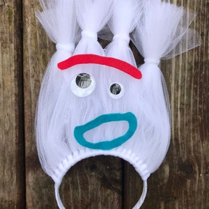 May include: White tulle headband with a red, blue, and white felt face. The face has two large white eyes, a red eyebrow, and a blue mouth.
