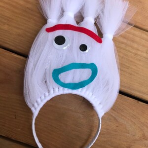 May include: White tulle headband with a felt face, red eyebrows, googly eyes, and a turquoise mouth.