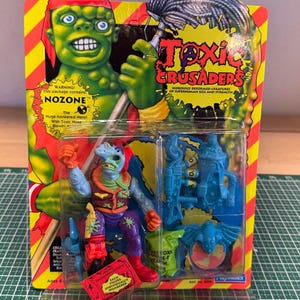 May include: A vintage Toxic Crusaders action figure in its original packaging. The figure is a green mutant with blue skin, wearing a vest and boots. The packaging features a cartoon illustration of the character and the words "Toxic Crusaders". Includes accessories.