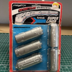 May include: A Midgetoy die-cast Amtrak Superliner train set in original red and blue packaging. The set includes five silver-coloured metal train cars sealed in a clear plastic blister pack. The card features the text Midgetoy, Die Cast To Last, and Amtrak Superliner.