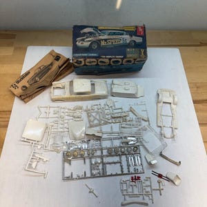 May include: A 1953 Studebaker model car kit including a blue and white cardboard box with the text 'Mr. Speed 53', a set of assembly instructions, and numerous unpainted white plastic parts and chrome-plated components attached to plastic frames.