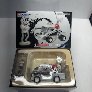 May include: A Corgi Classics James Bond Collection 007 Moon Buggy & James Bond figure set. The set includes a silver and black moon buggy with a red sphere and a figure of James Bond. The box features a black and white graphic.