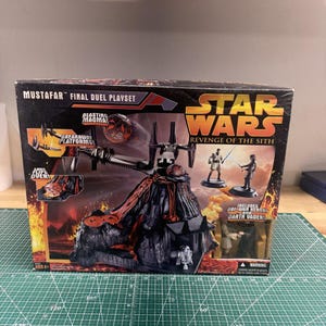 May include: A Star Wars: Revenge of the Sith Mustafar Final Duel Playset box. The box features a volcanic landscape with lava and figures of Obi-Wan Kenobi and Darth Vader. The box also includes the text "Blasting Magma" and "Breakaway Platforms."