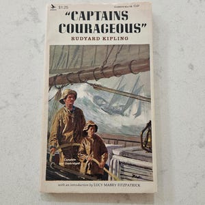 May include: A vintage paperback book titled "CAPTAINS COURAGEOUS" by Rudyard Kipling. The cover art depicts two figures on a ship during a storm. The book is complete and unabridged, with an introduction by Lucy Mabry Fitzpatrick.