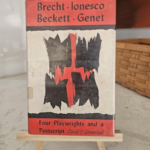 May include: A vintage book titled "Brecht • Ionesco Beckett • Genet" with a red and black cover design. The cover features a bold, abstract illustration and the text "Four Playwrights and a Postscript David J. Grossvogel". The book is displayed on a small wooden easel.