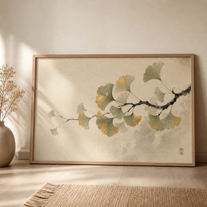 May include: A rectangular framed wall art print featuring a horizontal branch with fan-shaped ginkgo leaves in shades of muted green and yellow. The artwork is set against a textured cream background with a small red stamp in the bottom corner.