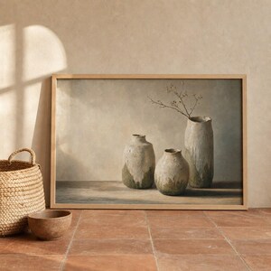 May include: A framed wall art print depicting three textured, neutral-toned ceramic vases on a flat surface. The tallest vase contains a single thin, bare branch. The vases feature a mottled, earthy finish with subtle green and beige color variations.