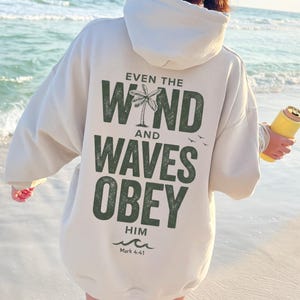 以下が含まれることがあります： 背面に「EVEN THE WIND AND WAVES OBEY HIM」というダークグリーンの掠れた文字がプリントされたベージュのパーカー。WINDの「I」の文字はヤシの木のグラフィックに置き換えられており、小さな鳥のシルエットと下部に「Mark 4:41」の文字がデザインされています。