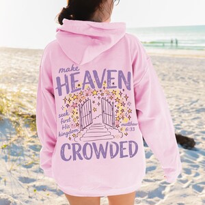 以下が含まれることがあります： 背面に紫色の「make HEAVEN CROWDED」という文字がプリントされたライトピンクのパーカー。デザインには、開いた門、階段、黄色い星のイラストと、「seek first His kingdom」、「matthew 6:33」というテキストが含まれています。