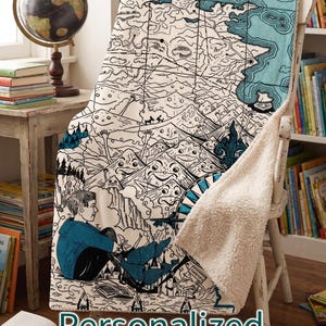 May include: A cream-colored blanket with a map-like illustration in black and teal, draped over a white chair. The blanket features a drawing of a person and the words "Personalized Storybook Blanket".