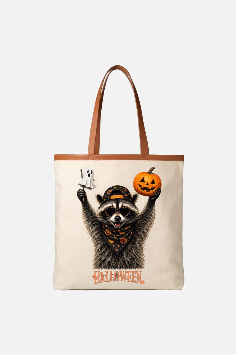 May include: A cream-colored tote bag with brown handles featuring a graphic of a raccoon wearing a baseball cap, heart-shaped sunglasses, and a patterned bandana. The raccoon holds a ghost and a jack-o'-lantern, with the word HALLOWEEN below.