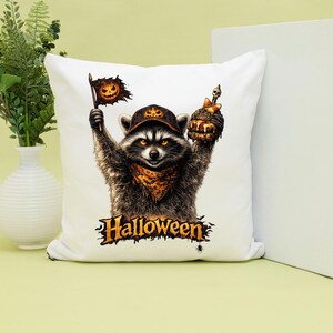 May include: A white square throw pillow featuring a graphic of a raccoon wearing a pumpkin-patterned cap and bandana. The raccoon holds a pumpkin flag and a burger topped with a skull. The word Halloween is printed in orange below the raccoon.