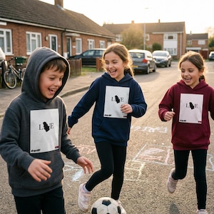 May include: Three children wearing hooded sweatshirts with the word "LOVE" and a graphic on the front. The sweatshirts are in charcoal grey, navy blue, and burgundy. The children are playing with a football on a street.