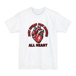 May include: A white short-sleeve t-shirt featuring a graphic of a red anatomical heart integrated with mechanical gears and a lightning bolt. The text reads PART HUMAN PART MACHINE in an arc above and ALL HEART in bold letters below the heart.