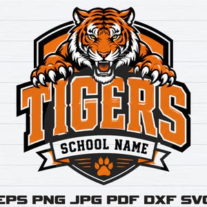 May include: A graphic logo design featuring a snarling tiger with orange and black fur, positioned above the word TIGERS in bold orange letters. Below this, the text SCHOOL NAME appears above an orange paw print on a black shield emblem.