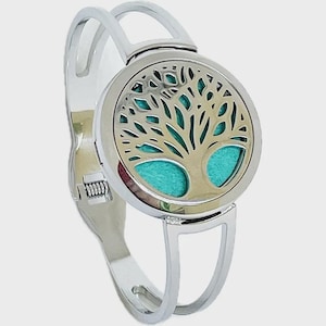 Peut inclure: Bracelet argenté avec un pendentif rond représentant un arbre de vie. L'arbre est doré, sur un fond turquoise. Le bracelet a un fermoir à charnière et un design minimaliste et ouvert.