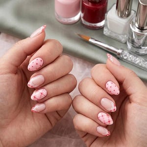 Könnte beinhalten: Manikürte Fingernägel mit einer Mischung aus Nagelkunst-Designs, darunter rosa Punkte, weiße Spitzen im Spitzen-Stil und ein rot-weißes Karomuster. Die Nägel sind oval geformt und werden neben vier Glasflaschen mit Nagellack präsentiert.