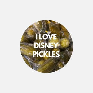 May include: A circular graphic featuring a collection of green pickles individually wrapped in clear plastic. The text I LOVE DISNEY PICKLES is printed in bold white capital letters across the center of the image over the pickles.