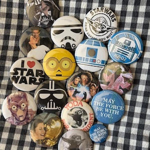 May include: A collection of Star Wars themed buttons. The buttons feature characters like Darth Vader, Yoda, and R2-D2. Some buttons have text like "Star Wars" and "May the Force be with you."