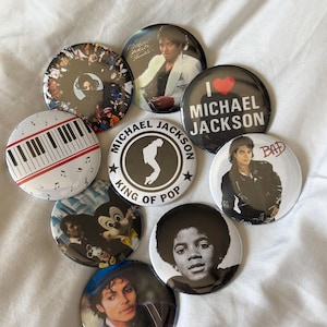 May include: A collection of round buttons featuring images of Michael Jackson. The buttons display various portraits, album art, and text, including "I Love Michael Jackson" and "King of Pop". The buttons are white, black, and various colors.