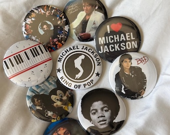 Op de afbeelding: Een verzameling ronde buttons met afbeeldingen van Michael Jackson. De buttons tonen verschillende portretten, albumhoezen en tekst, waaronder "I Love Michael Jackson" en "King of Pop". De buttons zijn wit, zwart en in diverse kleuren.