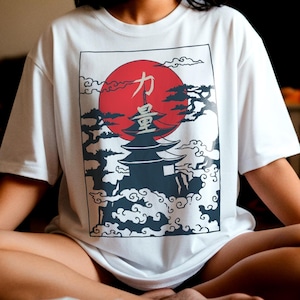 Può includere: T-shirt bianco con un design di ispirazione giapponese, con un sole rosso, una pagoda e nuvole stilizzate. La grafica include caratteri giapponesi. La maglietta è uno stile casual a maniche corte.