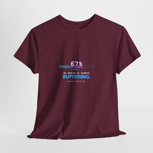 May include: Burgundy t-shirt with the text "67% Loading... My Brain is Always Buffering. Please Stand By." The text is in white and blue, with a loading bar graphic above the text. The shirt is a crew neck and has short sleeves.