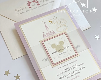 May include: A pink and gold wedding invitation with a Mickey Mouse silhouette and the text "Rebecca & Marcus" and "May 7, 2022". The invitation features a pink and gold castle with a fairy flying above it. The invitation also includes the text "as they exchange marriage vows" and "Saturday, May 7, 2022 at twelve o'clock in the afternoon" and "Disney's Wedding Pavilion, Orlando, Florida".