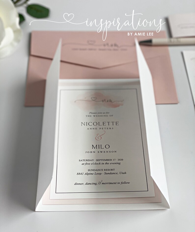 May include: Wedding invitation suite featuring a white and blush pink color scheme. The invitation includes the names Nicolette and Milo, the wedding date, time, and location. The text "inspirations by Amie Lee" is at the top.