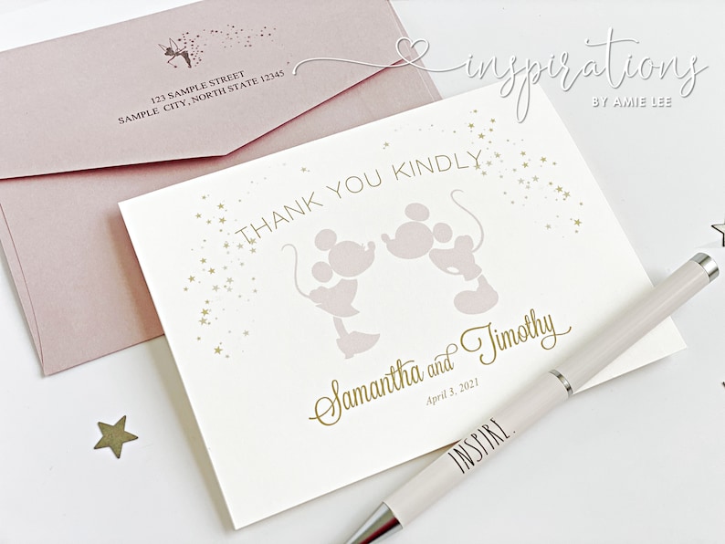 Puede incluir: Una tarjeta crema con letras doradas y un dise&ntilde;o de Mickey y Minnie Mouse, junto con un sobre rosa rubor. La tarjeta dice "Thank You Kindly" y "Samantha and Timothy, April 3, 2021." Tambi&eacute;n hay un bol&iacute;grafo con la palabra "INSPIRE".