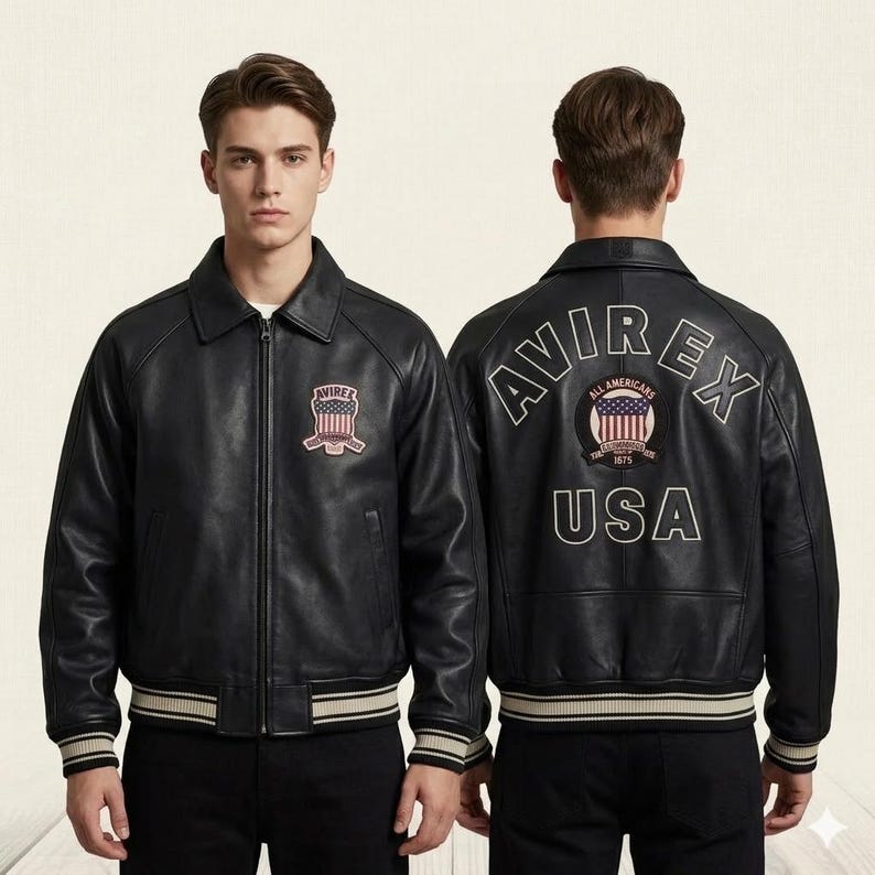 Puede incluir: Una chaqueta de cuero negra con cuello vuelto, cremallera frontal y pu&ntilde;os y dobladillo de canal&eacute; a rayas. El frente presenta un parche de bandera Avirex USA. La parte posterior muestra el texto Avirex, un parche circular de bandera y USA.