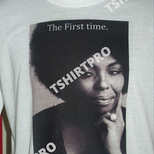 May include: A white t-shirt with a black and white photo of a woman with an afro. The text "The First Time." is printed above the photo. The woman's name, "Roberta", is written in cursive below the photo.