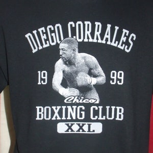 May include: Black t-shirt with a white graphic of a boxer, the text "Diego Corrales 19 99 Chico's Boxing Club XXL" and a white outline of a boxing ring.