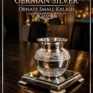 May include: A small German silver kalash featuring intricate floral engravings on its rounded body and a flared rim. The vessel rests on a square, mirrored base with a metallic frame. Text on the image reads GERMAN SILVER ORNATE SMALL KALASH.
