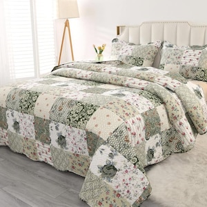 May include: A patchwork quilt and two matching pillow shams featuring a repeating pattern of floral prints, damask motifs, and small geometric designs in shades of sage green, cream, white, and muted pink, draped over a bed with a headboard.