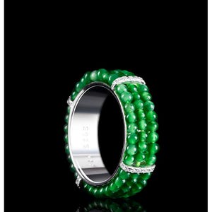 May include: A ring featuring three parallel rows of small, round, green beads set against a polished silver band. The band is stamped with S925, indicating sterling silver. The design includes small, silver-toned accents embedded with clear stones.