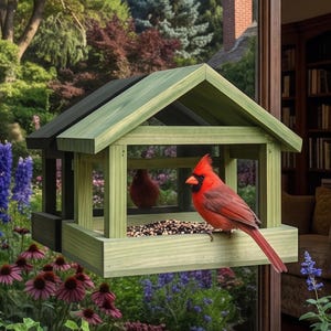 May include: A light green wooden bird feeder attached to a window pane. The feeder has a peaked roof and an open design, containing a mix of seeds. A bright red cardinal bird is perched on the edge of the feeder, facing toward the left side.
