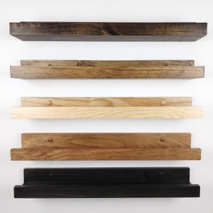 May include: Five horizontal wooden floating shelves arranged in a vertical stack. Each shelf features a rectangular backboard and a front ledge. The wood finishes vary from dark espresso and medium brown to light natural wood and solid black.