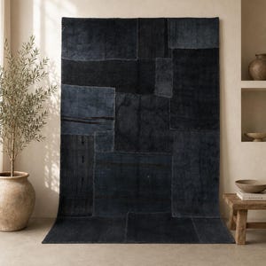 Puede incluir: Una alfombra rectangular grande con un diseño de retazos en varios tonos de azul oscuro. La alfombra está hecha de múltiples piezas rectangulares cosidas con costuras visibles. La alfombra se exhibe sobre un suelo de color claro.