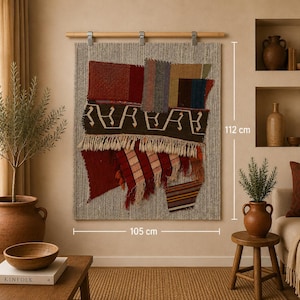 Peut inclure: Une tenture murale tissée, de 105 cm de large et 112 cm de haut, avec un fond gris texturé et des patchs colorés rouges, bruns et bleus. Le design comprend un bas à franges et un motif décoratif.