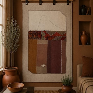 May include: A rectangular wall hanging made of beige linen fabric featuring a central patchwork design with geometric patterns in red, brown, and dark purple, suspended from a wooden rod by four black leather straps with metal hardware.
