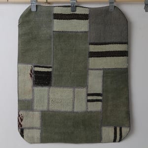 Può includere: Un tappeto rettangolare patchwork con un bordo superiore arrotondato. Il tappeto presenta una varietà di toppe rettangolari e quadrate in tonalità di verde, grigio e crema. Alcune toppe hanno strisce nere e crema. Il tappeto è appeso a un'asta di legno.