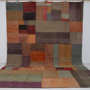 May include: A large rectangular area rug featuring a patchwork design composed of various fabric segments in muted tones of orange, brown, gray, purple, and red. The rug displays a grid-like arrangement of rectangular patches.